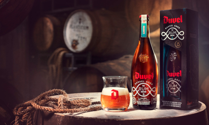 Duvel Barrel Aged Batch 5 The Rum Edition glas, fles en cadeauverpakking bovenop een rumvat